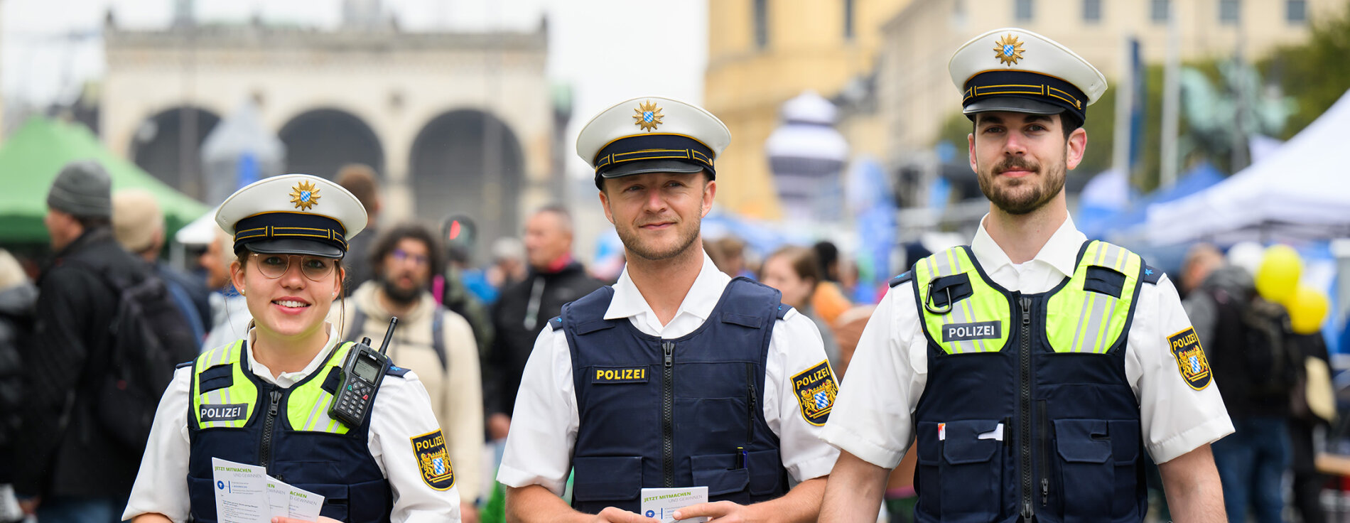 Gelungenes Straßenfestival der Bayerischen Polizei und 10. Landestag der Verkehrssicherheit: Ein attraktives Programm und spannende Einblicke in die Polizeiarbeit lockten zahlreiche Besucher an. 3 Polizistinnen und Polizisten auf Festival, im Hintergrund Festivalbesucher