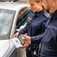Strafzettel im Straßenverkehr können mit der mOwi-App künftig leichter erfasst und bezahlt werden. Polizistin und Polizist beim Scannen des QR-Codes des Strafzettels mit dem Handy
