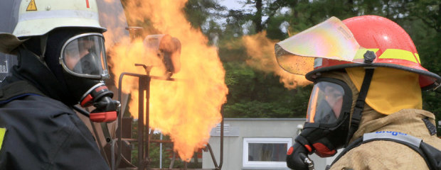 Zwei Feuerwehrleute. Dahinter ein großes Feuer. Zwei Feuerwehrleute. Dahinter ein großes Feuer.
