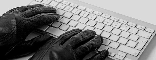 Ein Computer wird ausspioniert. Das Foto zeigt zwei Hände in schwarzen Lederhandschuhen die auf einer Computertastatur liegen.