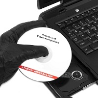 Von einem Computer werden Daten heruntergezogen. Das Foto zeigt ein Notebook mit geöffnetem CD-/DVD-Laufwerk; eine Hand in einem schwarzen Lederhandschuh entnimmt daraus eine CD/DVD mit der Aufschrift „Patente und Entwicklungsdaten – STRENG VERTRAULICH"